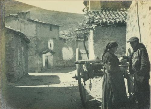 (Dos campesinos en la calle de un pueblo, junto a un carro)