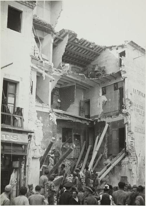 (Gente en una calle con una casa destruida en un bombardeo)